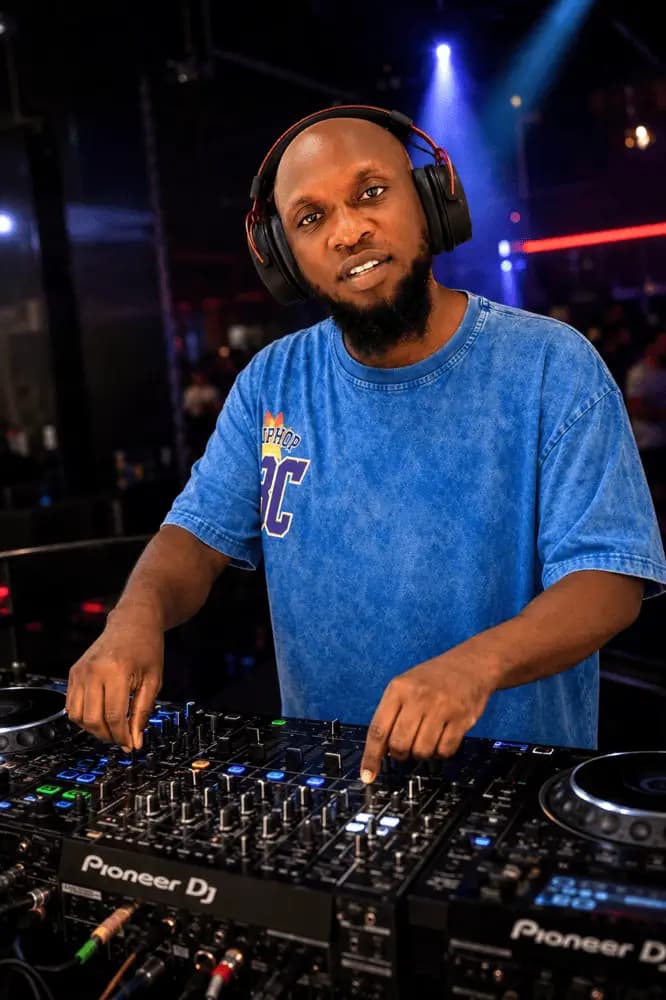 DJ TBLACK at the decks in a club, wearing headphones